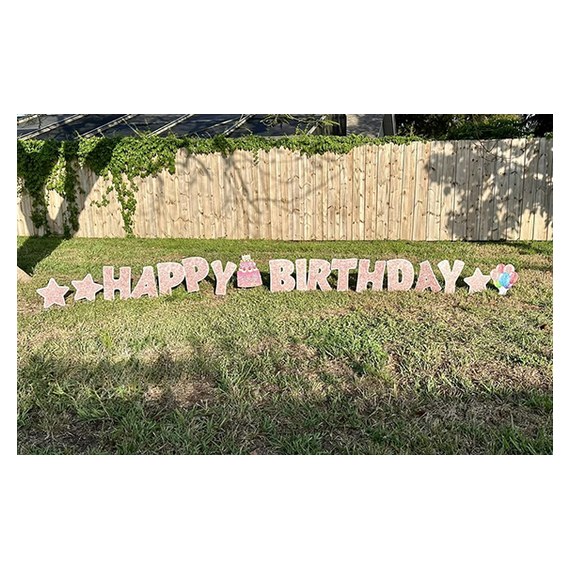 Happy Birthday yard letters set up on grass in front of a wooden fence