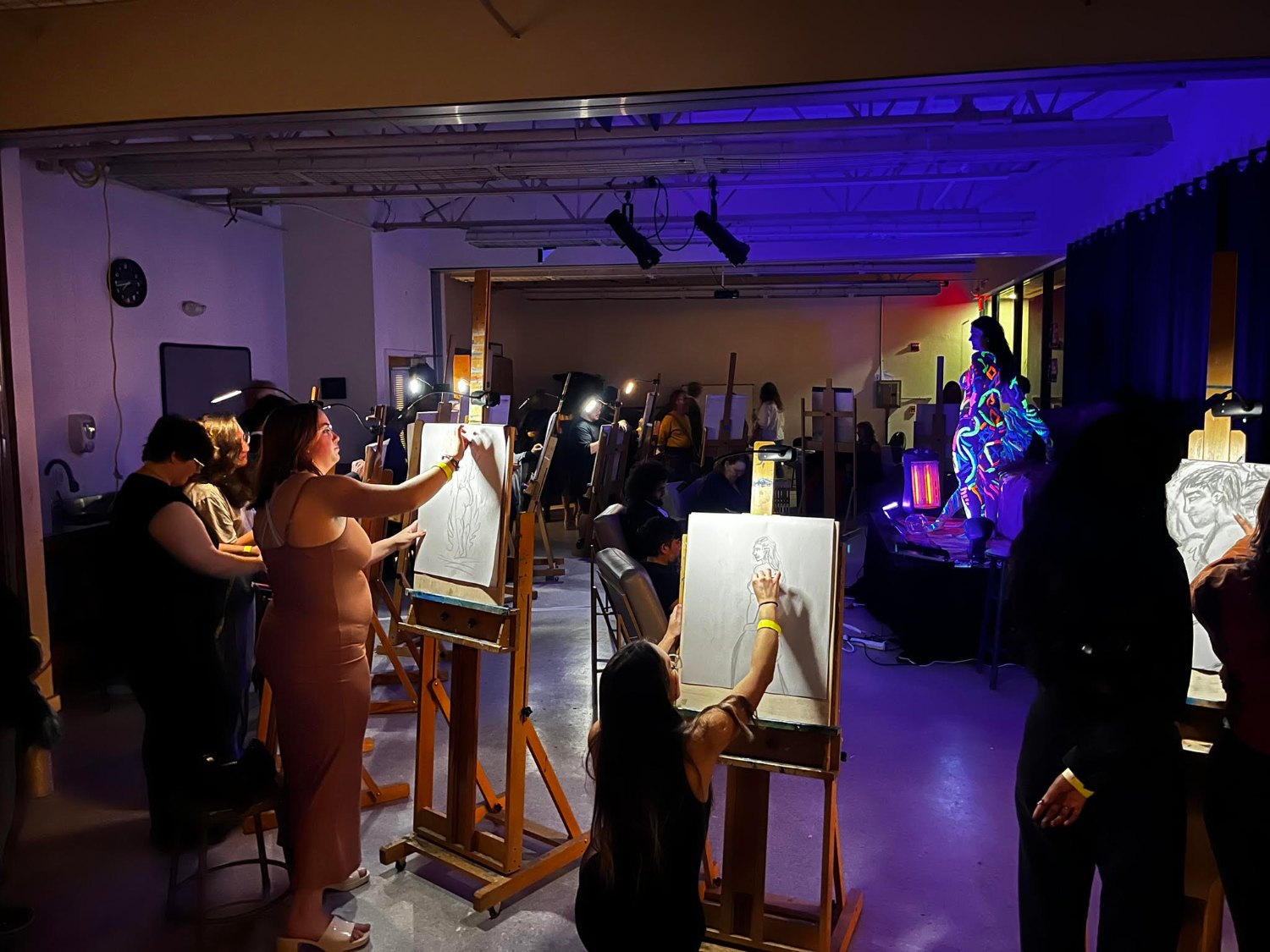 Guests at easels sketching a body-painted model under blue light